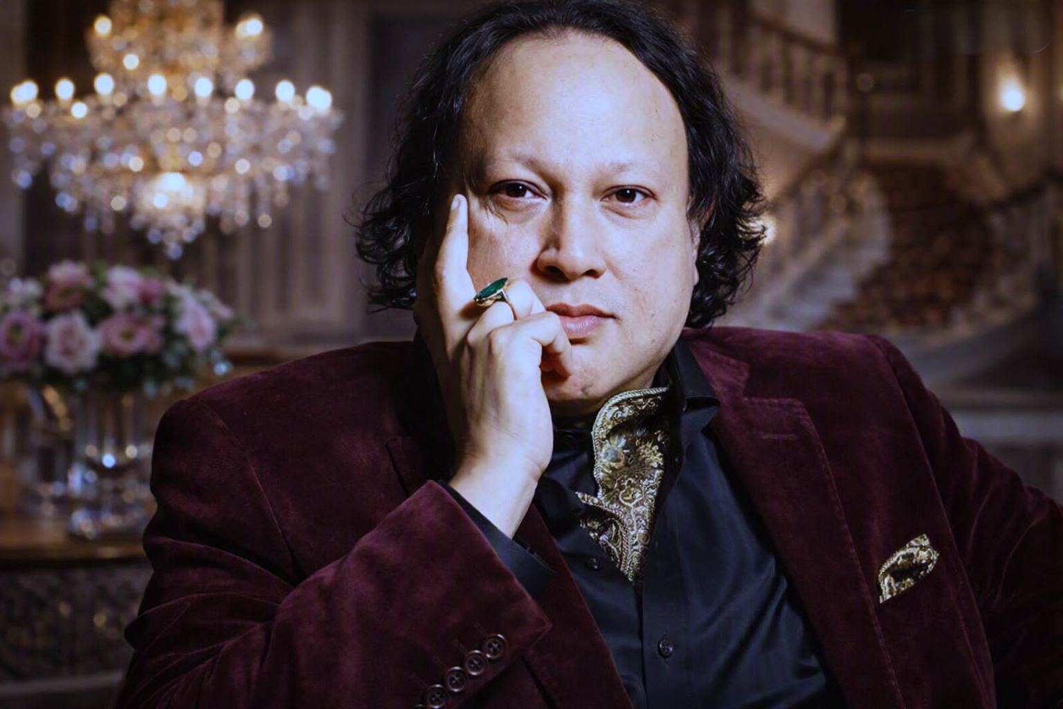 Brown velvet coat aur tie mein haath gaal par rakhe hue.