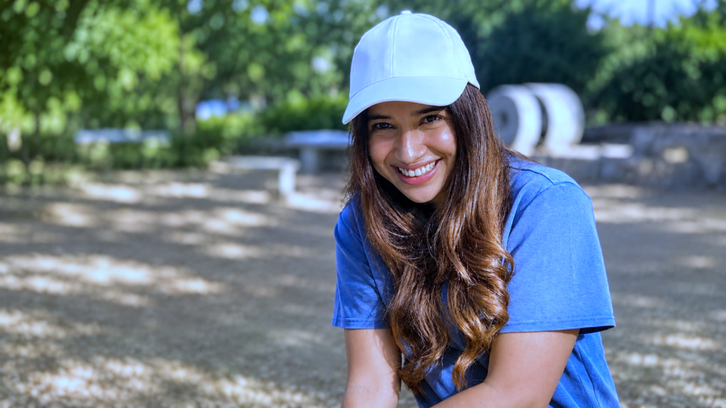 Blue T-shirt aur white cap mein outdoor smile