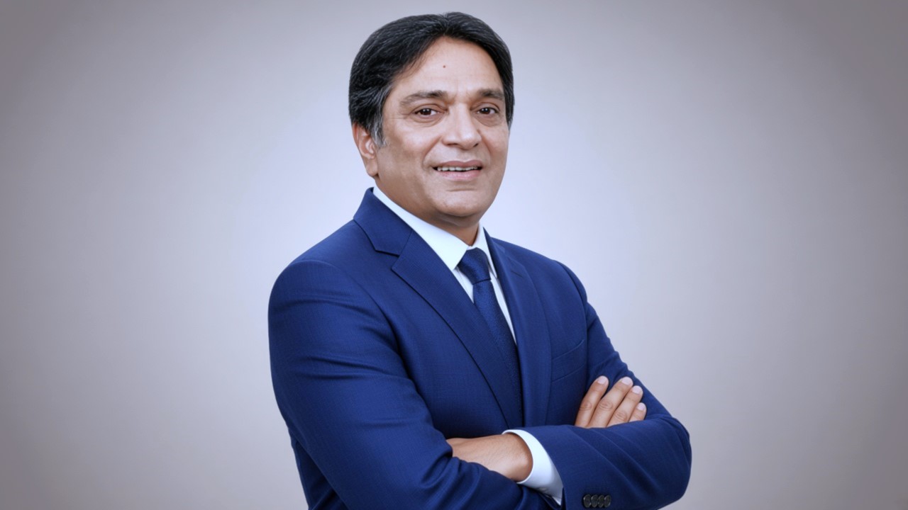 Famous South Asian comedian wearing a blue formal suit with folded arms 