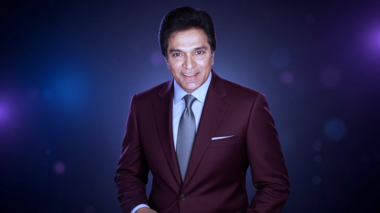 Smiling television superstar wearing a maroon blazer and tie under stage lights