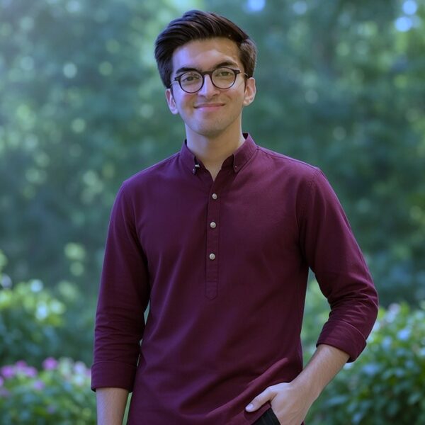 Smiling young actor wearing glasses and a traditional maroon kurta standing in a green garden